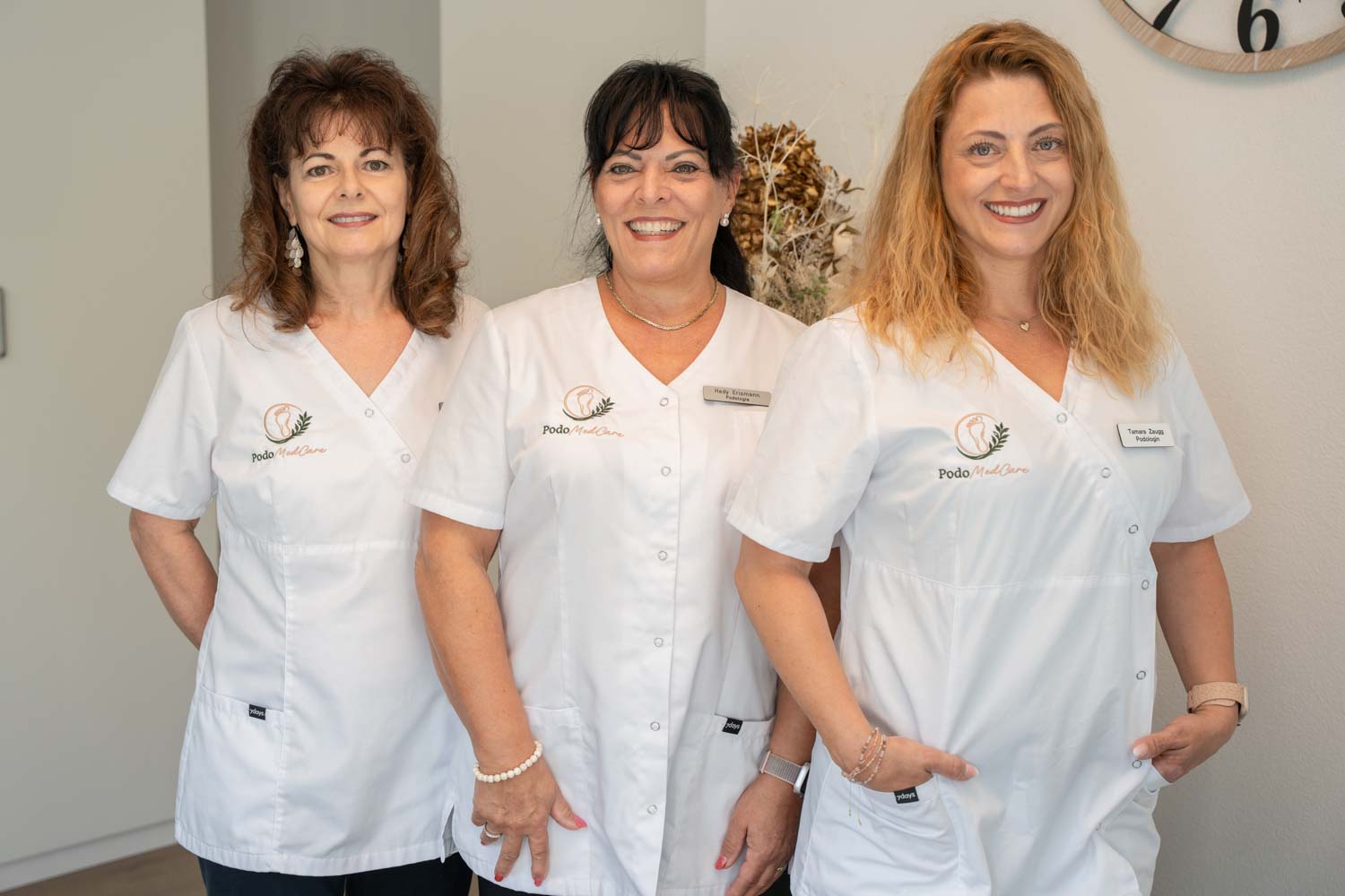 Das freundliche Team von podomedcare steht gemeinsam in der Praxis und lächelt in die Kamera.